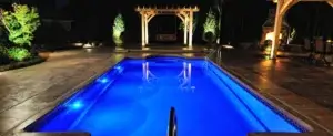 Nighttime view of a backyard patio with a pool, pergola, and beautifully illuminated landscaping, creating a resort-like atmosphere | Midwest Lightscapes